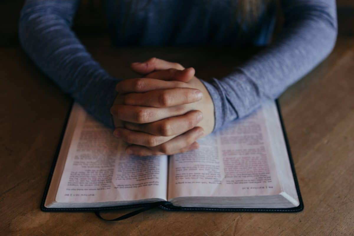 Crossed hands over a bible for prayer at Adult & Teen Challenge